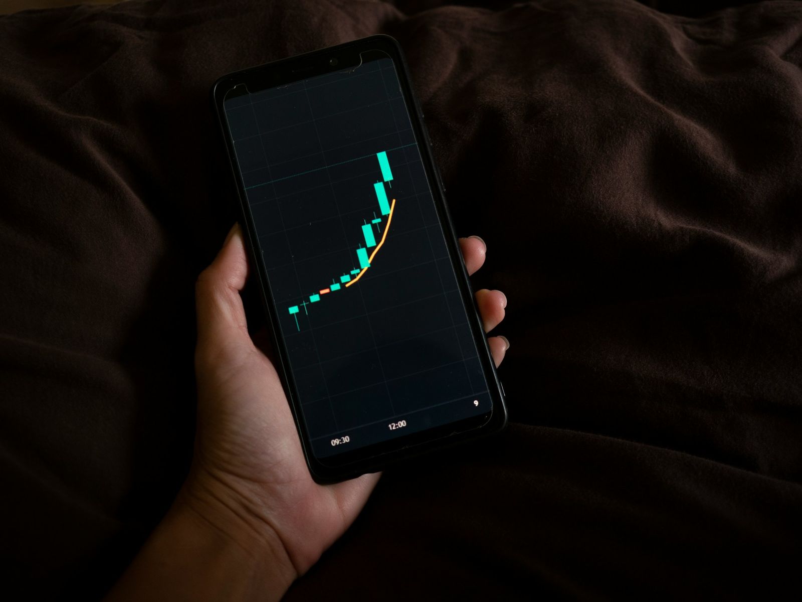 Hand holding a smartphone displaying a steep upward candlestick chart, indicating rapid market growth.