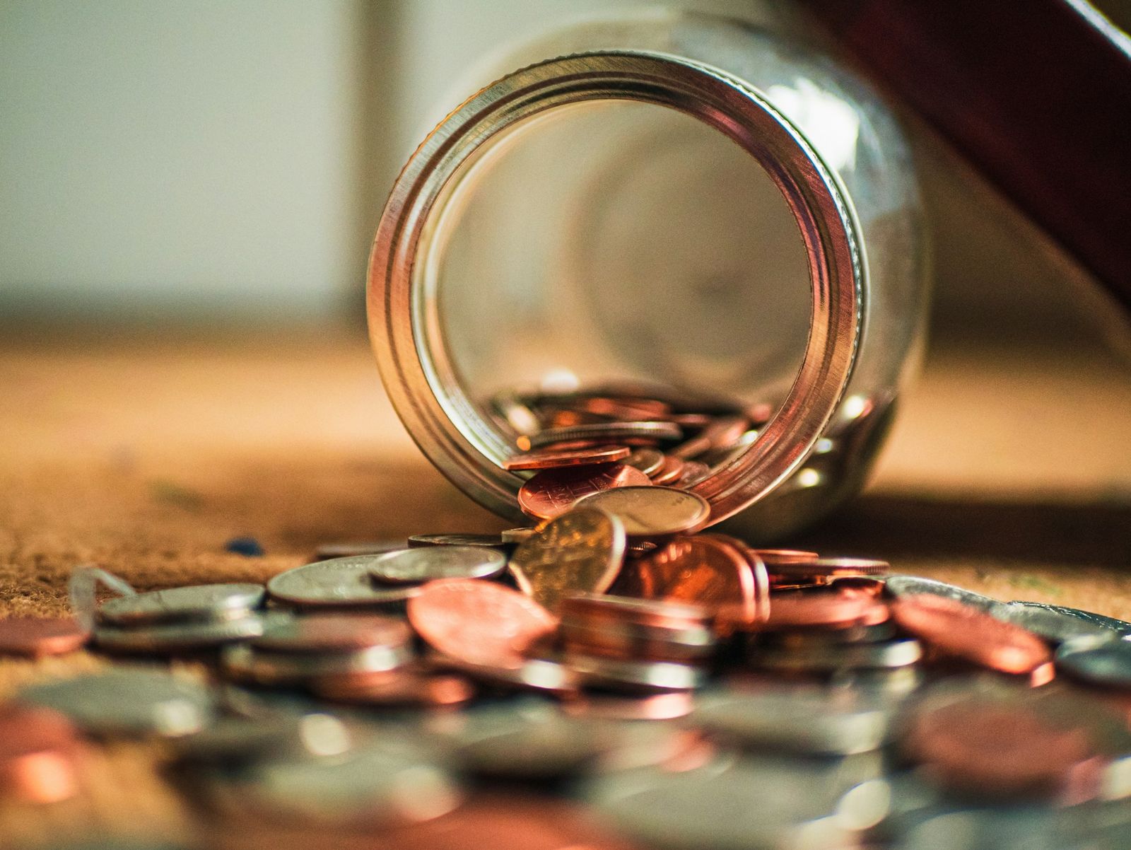 Glass jar tipped over with coins spilling out onto a surface, symbolizing savings, budgeting, or financial planning.